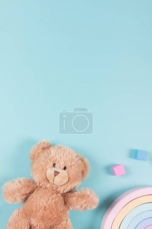 Baby kids educational toys background. Teddy bear, wooden toy rainbow and colorful blocks on light blue background. Top view, flat lay.