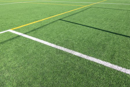 Photo for White and yellow stripes on green soccer field from side view. Artificial turf on football field. Green synthetic grass on sport ground with shadow from soccer goal net. - Royalty Free Image