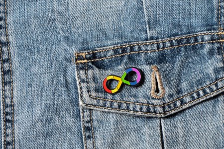 Photo for World autism awareness day. Closeup view of denim jacket with metallic pin brooch. Autism infinity rainbow symbol sign. Autism rights movement, neurodiversity, autistic acceptance movement symbol sign - Royalty Free Image