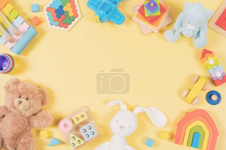 Baby Kinder Spielzeugrahmen Hintergrund. Teddybär, buntes pädagogisches, musisches, sensorisches, sortierendes und stapelbares Spielzeug für Kinder auf gelbem Hintergrund. Draufsicht, flache Lage.