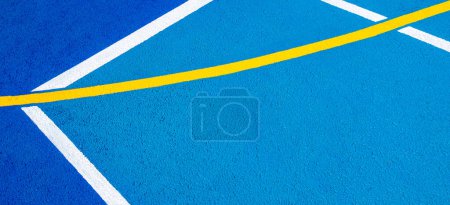 Téléchargez les photos : Terrain de sport fond. Surface du sol bleu caoutchoutée et granulée avec des lignes blanches et jaunes sur le sol. Vue du dessus. - en image libre de droit