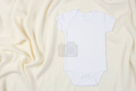 Foto de Vista superior al body de manga corta de algodón blanco sobre fondo de manta beige. Una maqueta de un bebé. Plantilla de maqueta de traje de recién nacido neutro de género en blanco. - Imagen libre de derechos