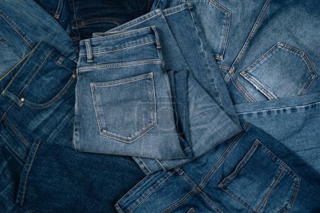 Denim background. Pile of blue jeans. Variety of casual trousers and clothes. Top view to stack of jeans denim.