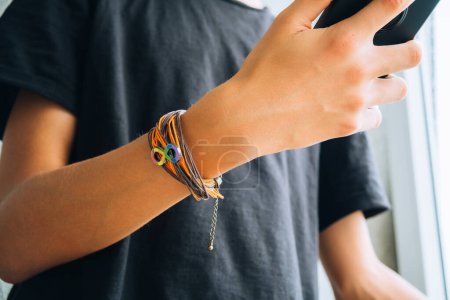 Photo for Teenage boy using smartphone. Wristlet with autism infinity rainbow symbol sign on his hand. World autism awareness day, autism rights movement, neurodiversity, autistic acceptance movement. - Royalty Free Image