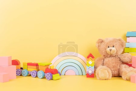 Educational kids toys collection. Teddy bear, wood rainbow, xylophone, wooden educational baby toys on yellow background. Front view.