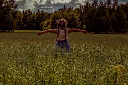 Ein Mädchen genießt die Sommersonne in einem Kornfeld zur Sommersonnenwende. Ein Blumenkranz schmückt den Kopf.