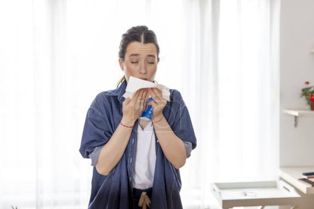 Close up sick young woman blowing running nose, sneezing, holding paper napkin, feeling unwell, female suffering from seasonal allergy symptoms, respiratory disease, cold or flu