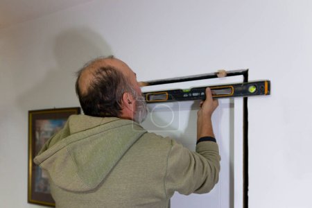 A worker's hands with  spirit level against frame of  the door. An experienced mature carpenter  installing interior door with a wooden frame at new  apartment. 