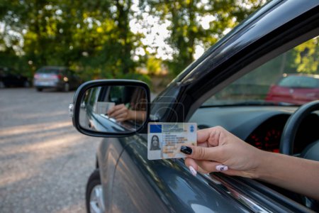Téléchargez les photos : Adolescente montrant son permis de conduire dans la fenêtre de la voiture après avoir passé l'examen ou à la demande de la police de la circulation - en image libre de droit