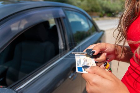 Téléchargez les photos : Adolescente montrant son permis de conduire dans la fenêtre de la voiture après avoir passé l'examen - en image libre de droit