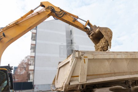 Gran excavadora está llenando un camión volquete con tierra en el sitio de construcción, proyecto en curso.
