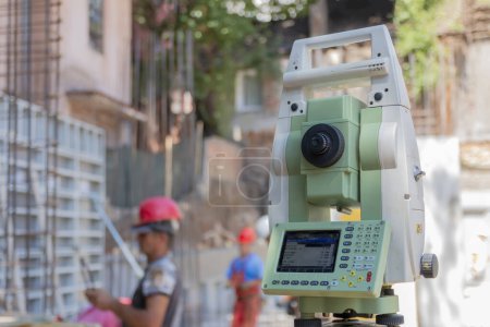Photo for Surveying measuring equipment level theodolite on tripod at construction site with workers in background - Royalty Free Image