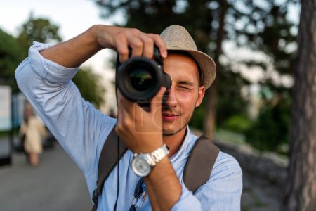 schöner junger Mann mit Rucksack und Hut auf Reisen und fotografiert die Stadt