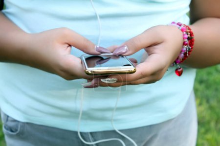 Vista de cerca de la mujer con uñas largas usando su teléfono inteligente en la naturaleza y escuchando música
