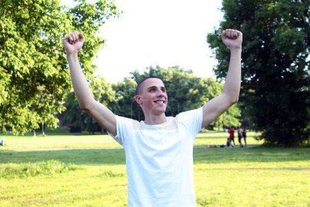 Young handsome teenager celebrating in the public park with raised hands