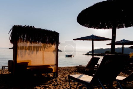 Sombrillas de paja y tumbonas en la playa sobre el fondo del mar al amanecer. Instalaciones relajantes. Vacaciones en la playa.