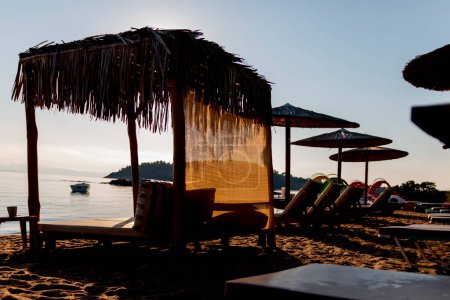 Sombrillas de paja y tumbonas en la playa sobre el fondo del mar al amanecer. Instalaciones relajantes. Vacaciones en la playa.
