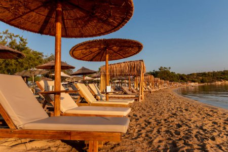 Straw umbrellas and sunbeds on the beach against the background of the sea at dawn. Relaxing facilities. Holidays on the beach.