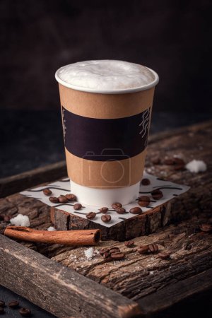 Foto de A cardboard glass with coffee on a wooden board, coffee beans are scattered on the board and a cinnamon stick lies - Imagen libre de derechos