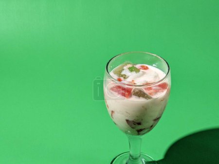 Fruit soup or mixed ice in a glass cup on a green background. Street fast food. Popular Indonesian fruit cocktail dessert