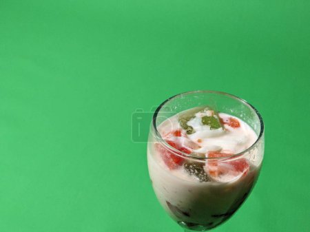 Fruit soup or mixed ice in a glass cup on a green background. Street fast food. Popular Indonesian fruit cocktail dessert