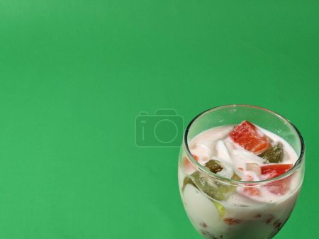Téléchargez les photos : Soupe de fruits ou glace mélangée dans une tasse en verre sur fond vert. Restauration rapide de rue. Populaire dessert aux fruits indonésien - en image libre de droit