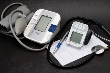 Foto de Tonómetro braquial, medidor digital automático de la presión arterial de la muñeca, estetoscopio, acostado en la mesa, diagnóstico de presión, sobre un fondo oscuro - Imagen libre de derechos
