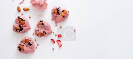 Photo for Heart-shaped candies with pink chocolate with strawberries, blueberries and almonds, handmade, top view, on white background, banner, place for text - Royalty Free Image