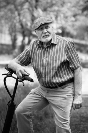 Foto de Un hombre positivo y anciano fue a dar un paseo por el parque, se detuvo y un scooter eléctrico estaba de pie junto a él. Verano, día soleado. Estilo de vida saludable de los mayores.Blanco y negro - Imagen libre de derechos