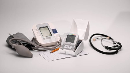 Foto de Monitor automático digital de muñeca y presión arterial braquial, gráfico de monitoreo de presión, pluma, gafas de estetoscopio sobre fondo blanco - Imagen libre de derechos