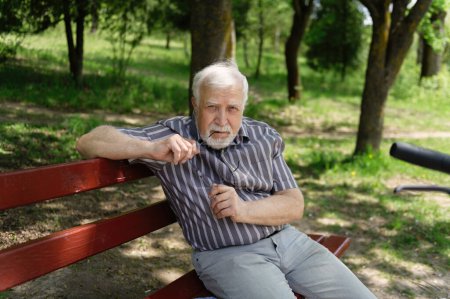 Photo for A positive, elderly man went for a walk to the park, stopped and sat down to rest on a bench next to an electric scooter. Summer, sunny day. Healthy lifestyle of the elderly. - Royalty Free Image