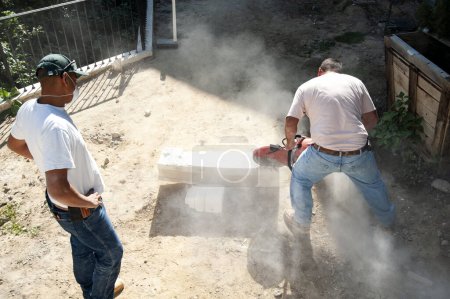 Stone masons using a concrete saw to cut a large piece of stone