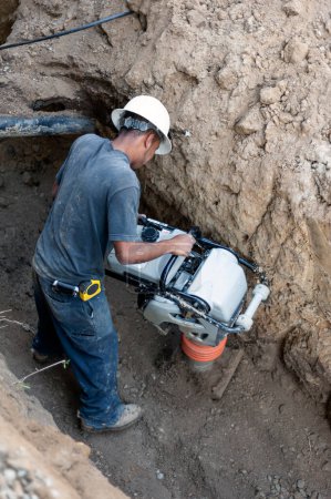 Construction worker using a compactor in a trench