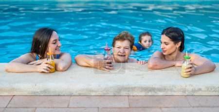 Téléchargez les photos : Belles et heureuses femmes d'âges différents qui s'amusent au bord de la piscine tout en buvant des boissons saines - en image libre de droit