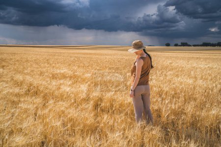 Foto de Vista trasera de la mujer mirando mientras está de pie en la cosecha contra el cielo nublado con tormenta y lluvia - Imagen libre de derechos