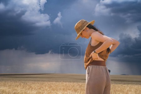 Téléchargez les photos : Vue arrière de la femme regardant debout en culture contre un ciel nuageux avec tempête et pluie - en image libre de droit