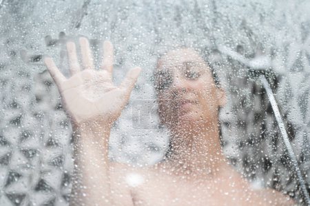 Téléchargez les photos : Femme douche à l'intérieur de la salle de bain, vue à travers le verre avec vapeur d'eau et gouttes - en image libre de droit