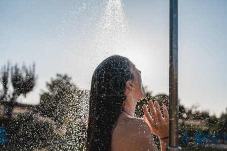 Téléchargez les photos : Belle jeune femme bénéficiant d'une douche extérieure au coucher du soleil - en image libre de droit