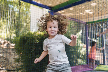 Téléchargez les photos : Joyeux petit garçon jouant sur une aire de jeux à l'extérieur à la lumière naturelle - en image libre de droit