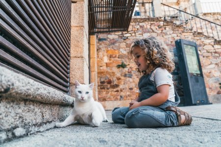 Téléchargez les photos : Mignon petit garçon jouer avec chat errant, concept de voyage - en image libre de droit