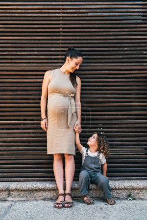 Photo for Pregnant woman and son looking at each other happy sitting on striped background - Royalty Free Image