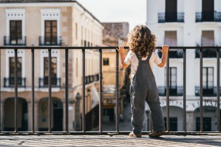 Foto de Fotografía horizontal de un niño mirando a la ciudad desde una terraza a través de una valla, turismo urbano - Imagen libre de derechos