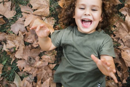 Foto de Niño feliz acostado jugando en la hierba con hojas secas - Imagen libre de derechos