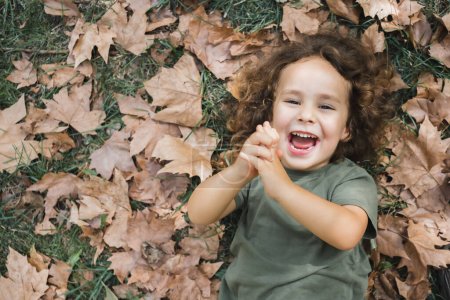 Foto de Niño feliz acostado jugando en la hierba con hojas secas - Imagen libre de derechos