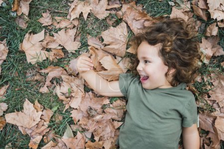 Foto de Niño feliz acostado jugando en la hierba con hojas secas, foto de perfil - Imagen libre de derechos