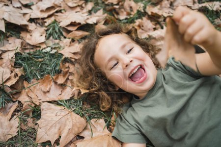 Photo for Happy child lying playing on the grass with dry leaves, closeup - Royalty Free Image
