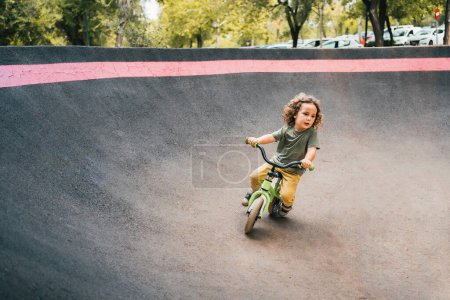 Téléchargez les photos : Heureux petit garçon style patineur entraînement avec son vélo sur circuit de piste de pompe - en image libre de droit