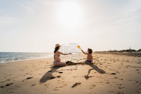 Photo for Mother and son playing in the sand on the beach at sunset against light - Royalty Free Image