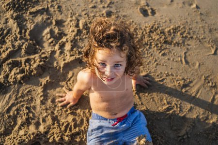 Téléchargez les photos : Portrait de petit garçon jouant avec le sable de la plage au coucher du soleil - en image libre de droit