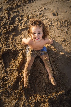 Téléchargez les photos : Portrait de petit garçon jouant avec le sable de la plage au coucher du soleil - en image libre de droit